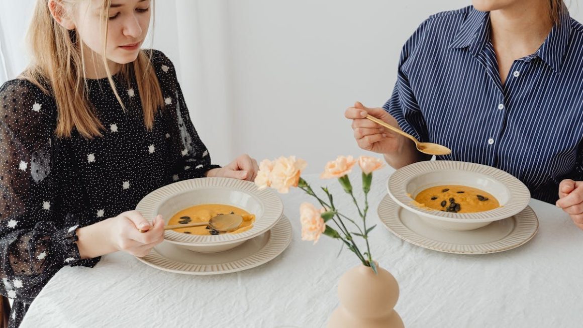 Two women enjoying homemade pumpkin soup at a dining table with floral decor.